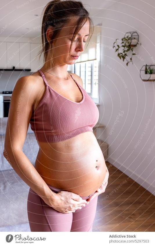Calm pregnant woman doing breathing exercise in living room yoga training eyes closed meditate zen home sportswear belly touch female young healthy lifestyle