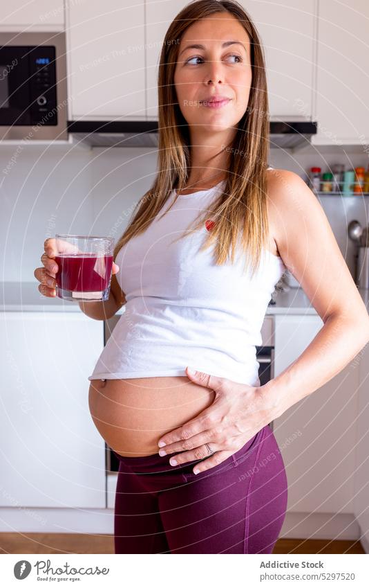Pregnant woman drinking juice in kitchen pregnant beverage expect pregnancy home belly female fresh healthy calm counter maternal tummy vitamin prenatal await