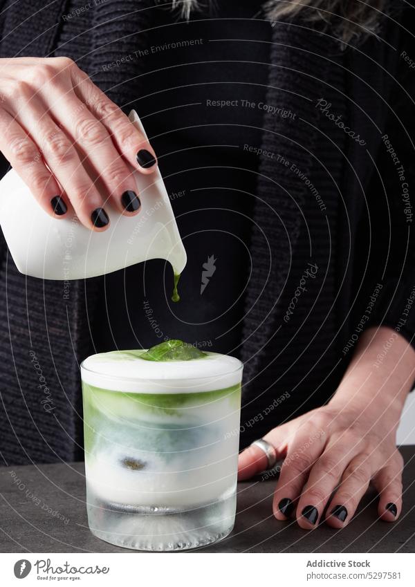 Unrecognizable woman pouring matcha in glass of milk drink ice prepare beverage add tea female fresh cup refreshment cold dairy healthy drink cocktail cube