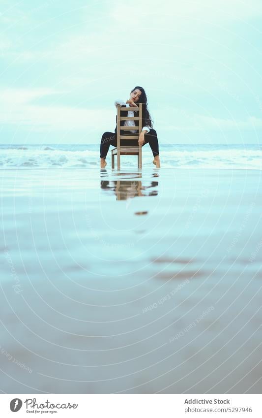 Thoughtful woman leaning on wooden chair in sea pensive calm thoughtful ocean rest appearance portrait female long hair young coast tranquil water personality