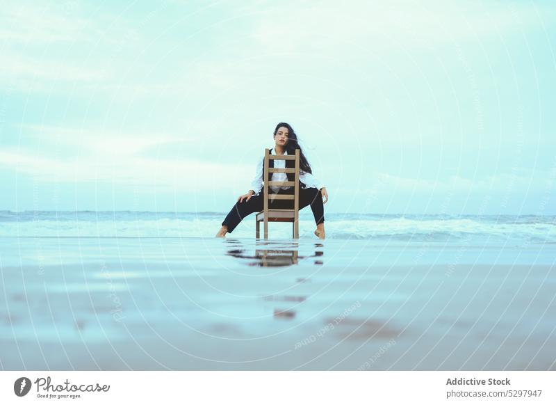 Thoughtful woman sitting on wooden chair in sea pensive calm thoughtful ocean rest appearance portrait female long hair young coast tranquil water personality