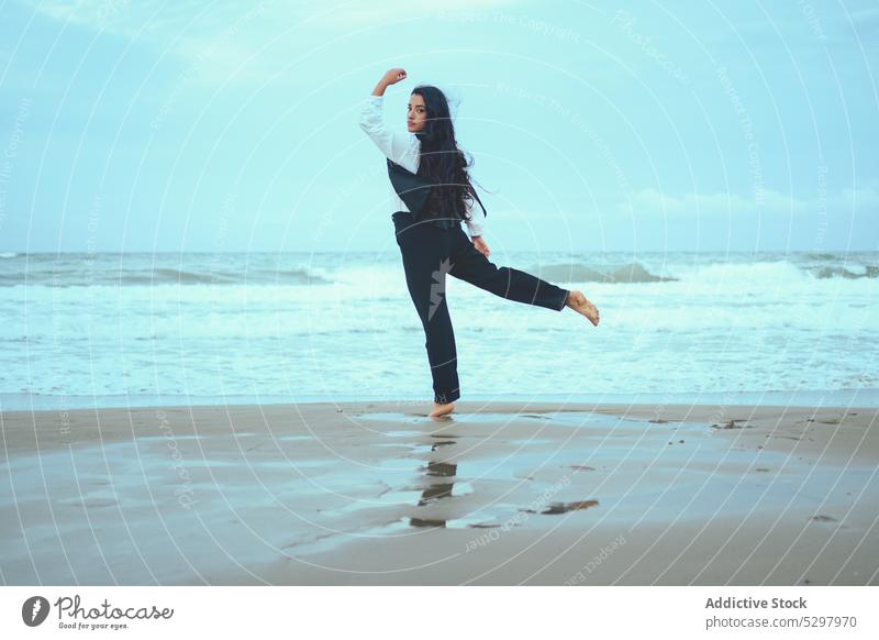 Graceful woman balancing on one leg on beach sea balance sand seashore wave outfit seaside summer coast barefoot ocean female water wet style harmony arm raised