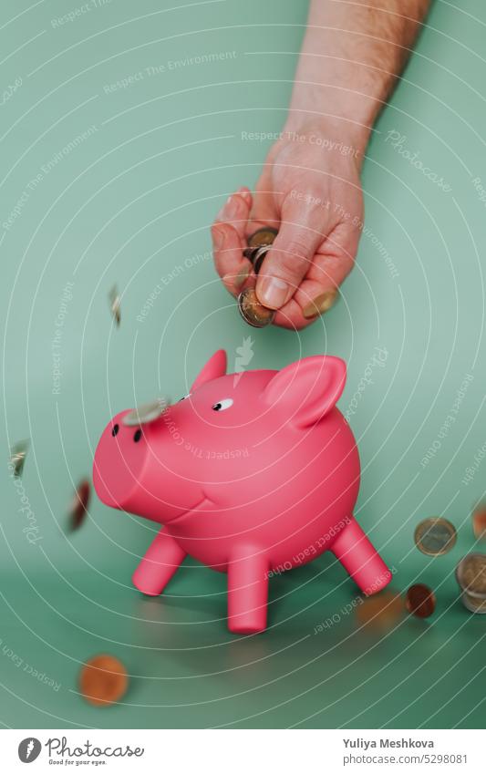 Falling euro coins from a male hand and a pink piggy bank on a green background.European Union money. Piggy Savings spending Hand concept finance currency cash