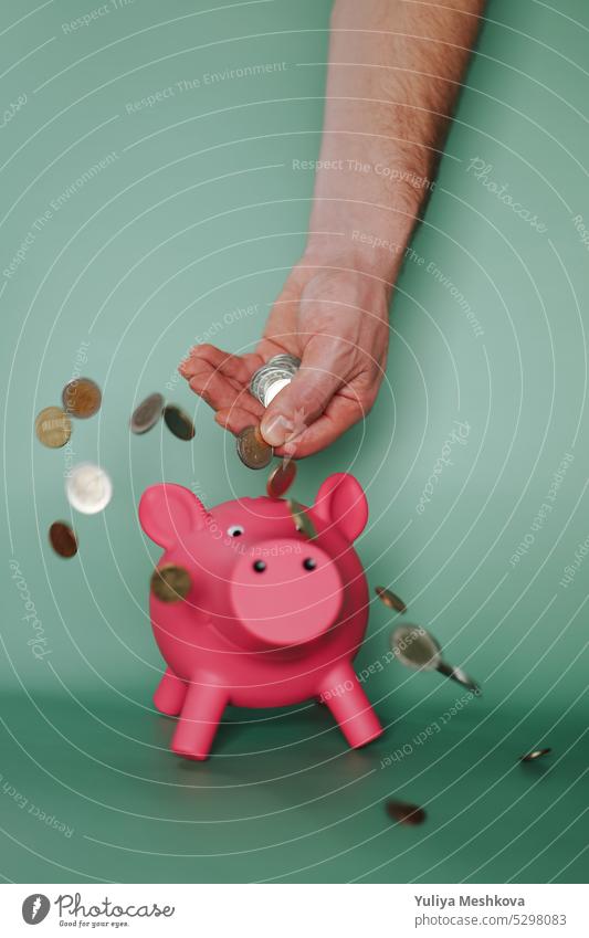 Piggy bank.Falling euro coins from a male hand and a pink piggy bank on a green background. Earnings and spending in the Eurozone. Savings Hand concept