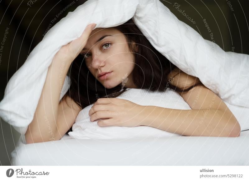 Portrait of an attractive, young, sexy brunette woman in bed, hand on the pillow and head under the blanket portrait copy space confident feminine brown white