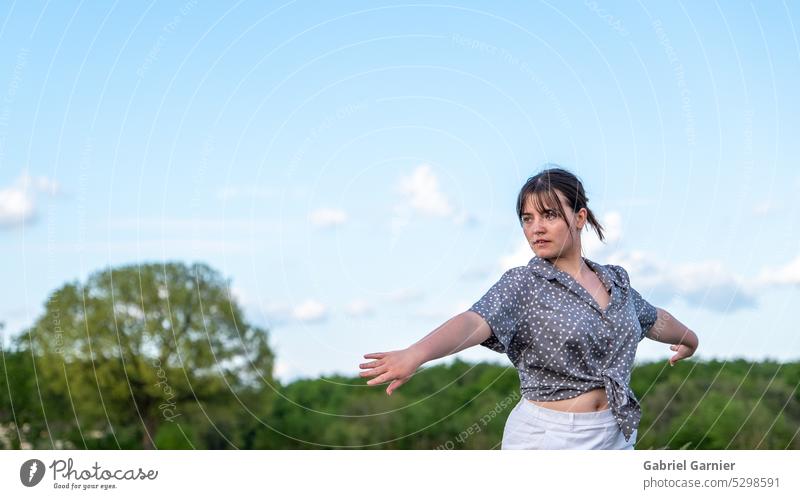 A beautiful young woman dances in nature, in front of the trees, with a blue and sunny sky. danse girl alone girl body people person personne profile