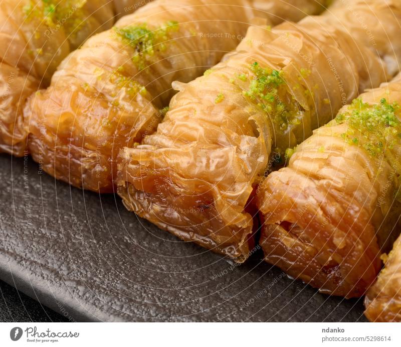 Pieces of baked baklava in honey and sprinkled with pistachios on a black board turkey sweet food pastry traditional arabic sugar dessert bakery baklawa syrup