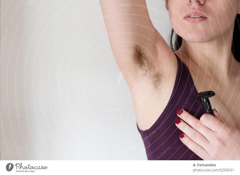 Detail of a woman holding a razor blade and showing her armpit hair. Woman with hairy armpit. Feminine beauty canons concept Armpit activist purple Uniqueness