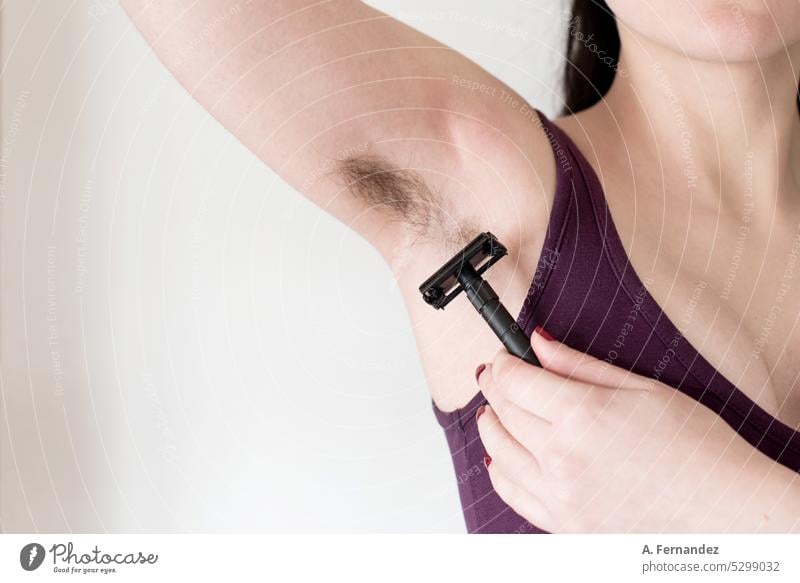 Detail of a woman using a razor blade to shave her armpit hair. Woman with hairy armpit. Feminine beauty canons concept Armpit Armpit hair female girl