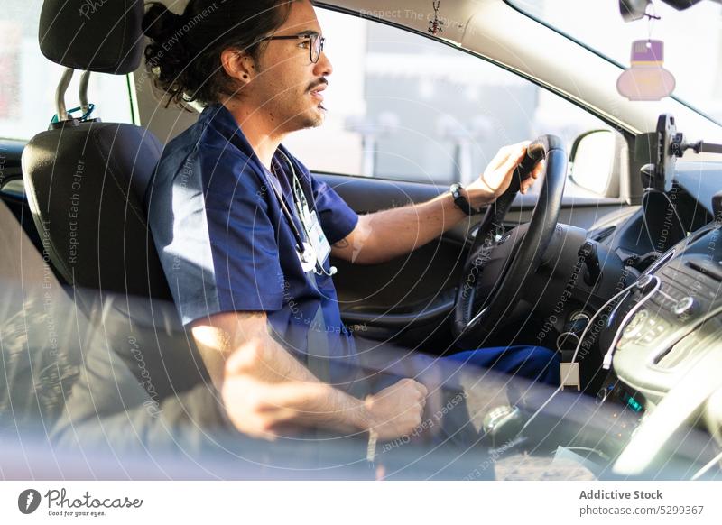 Concentrated ethnic man driving car in city doctor driver medical uniform work focus stethoscope vehicle professional job attentive eyeglasses occupation male