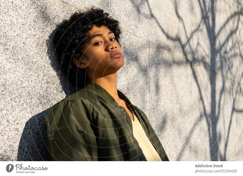 Serious young Asian man looking at camera in sunlight confident cool shadow portrait yellow appearance afro wall style ethnic hairstyle serious individuality