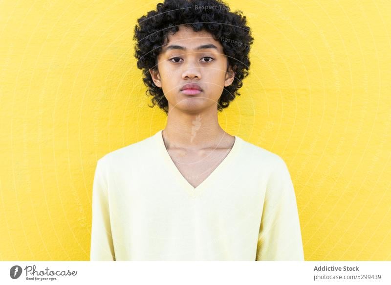 Serious young Asian man looking at camera in sunlight confident cool shadow portrait yellow appearance afro wall style ethnic hairstyle serious individuality