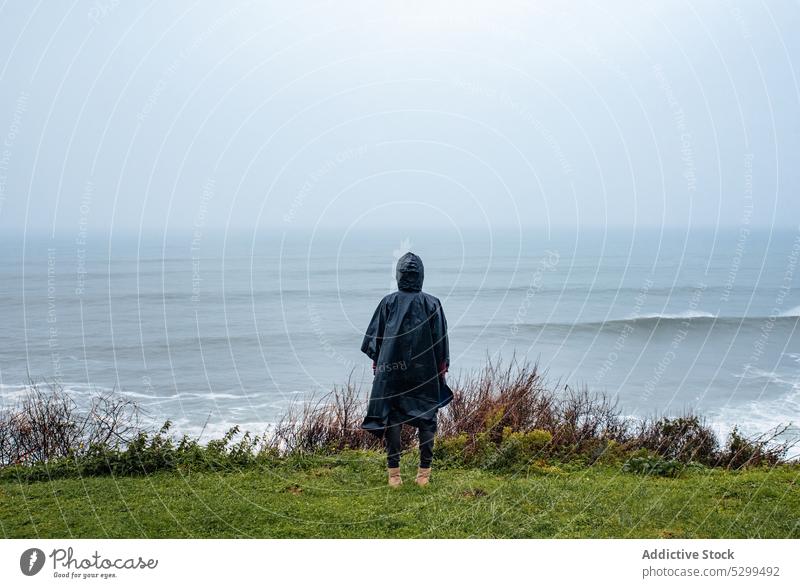 Anonymous hiker in raincoat admiring seascape woman traveler wave tourist admire nature storm stormy sky weather shore coast atmosphere ocean journey female