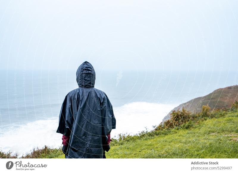 Anonymous hiker in raincoat admiring seascape woman traveler wave tourist admire nature storm stormy sky weather shore coast atmosphere ocean journey female