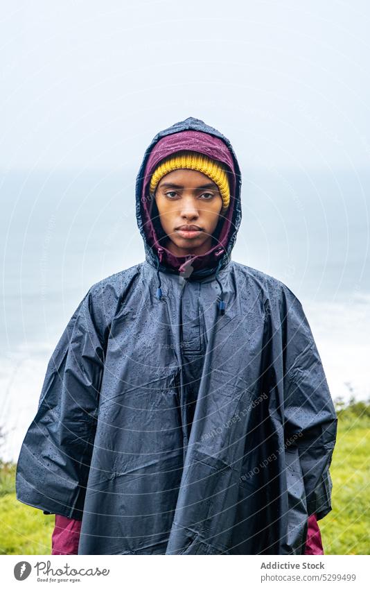 Serious woman in raincoat against ocean during trip hiker traveler vacation portrait serious tourist sea tourism nature cloudless female young journey coast
