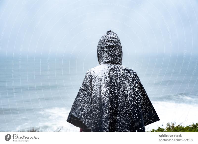 Faceless tourist in raincoat covered with snow traveler hoodie vacation explore admire nature sky stormy idyllic weather trip cloudless wanderlust alone harmony