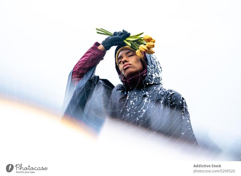 Black woman in raincoat with bouquet of flowers tulip eyes closed foam peaceful contemplate serious nature sky spring freedom female calm tranquil yellow relax
