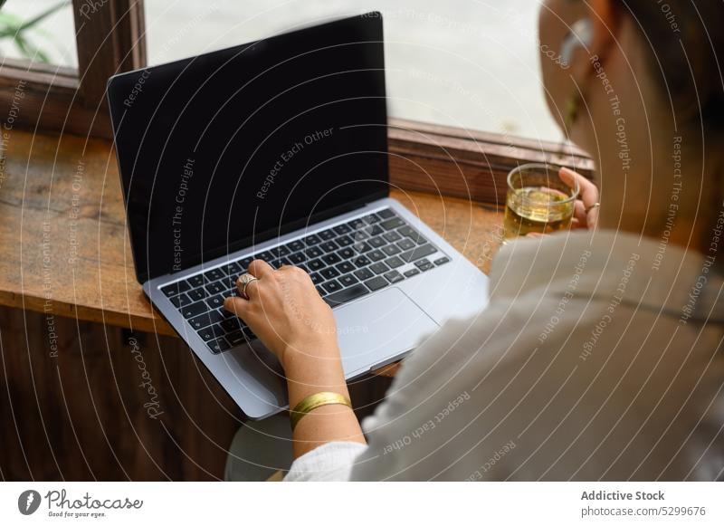 Anonymous woman typing on laptop in cafe remote freelance work drink using black screen tea female keyboard wireless vietnam gadget device earphones browsing