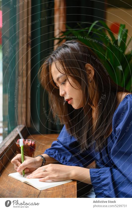 Concentrated Asian woman writing in notepad in cafe take note notebook student study drink concentrate write education female focus young thoughtful asian