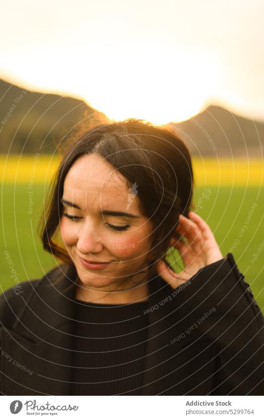 Smiling woman in green field positive lawn smile sunset countryside nature sky evening happy meadow female joy sundown young cheerful coat content carefree