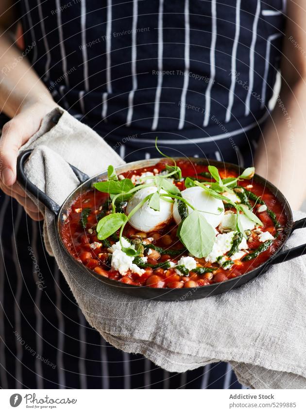 Woman with pan of delicious Shakshuka with Poached Eggs woman shakshuka egg poach chickpea tomato sauce feta cheese spinage female food meal dish tasty homemade