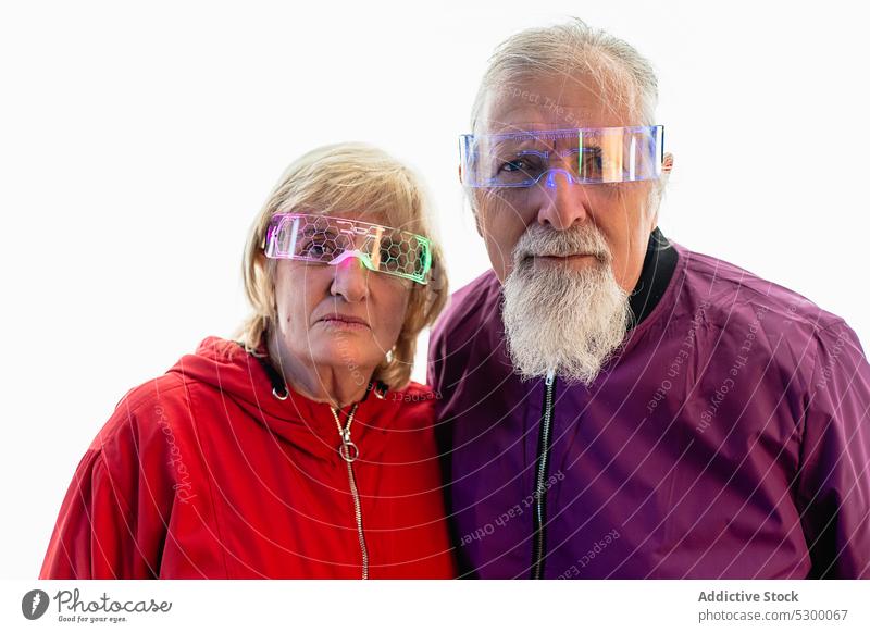 Senior couple standing near white wall and looking at camera serious confident pensive thoughtful relationship calm bright glasses together concentrate
