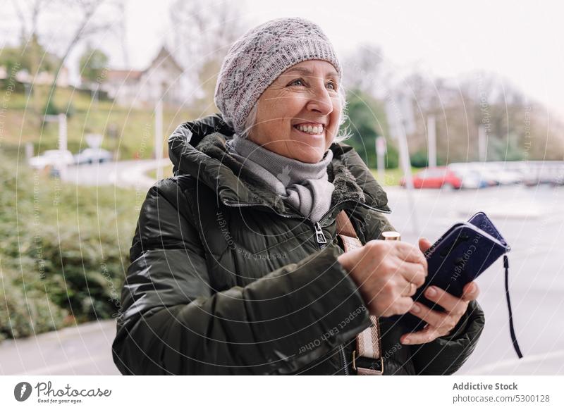 Cheerful senior woman with wallet on street smile positive happy city cheerful urban hat female mature warm clothes joy outfit lifestyle town daytime outerwear