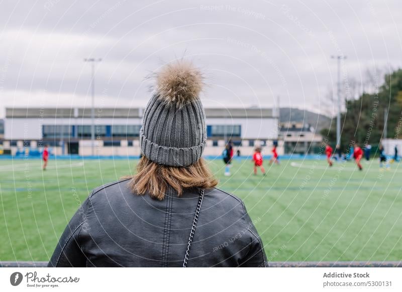 Unrecognizable woman in warm clothes watching football match field stadium sport game hat female daytime training competition soccer spectator player activity