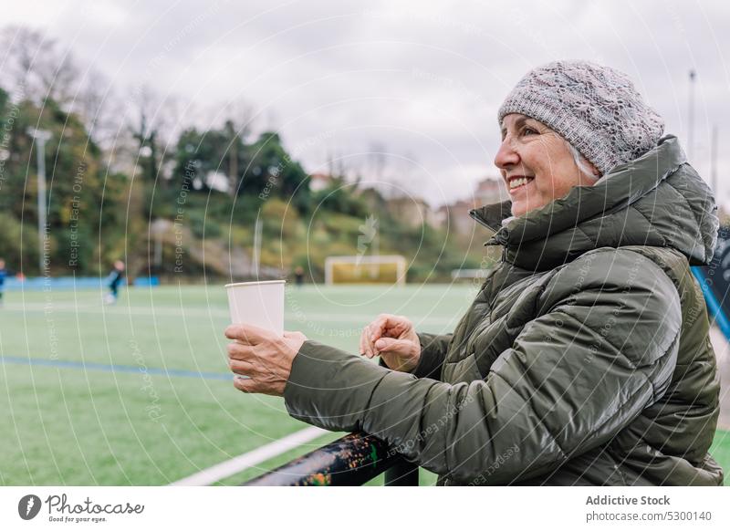 Joyful senior woman with takeaway coffee football match stadium happy cheerful drink smile cup female positive mature game to go sport enjoy delight content