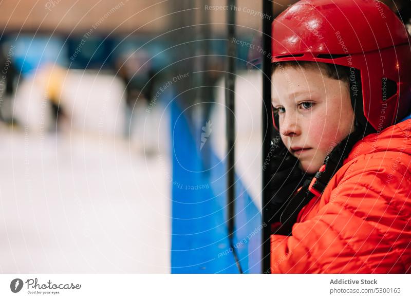 Pensive boy looking at ice rink winter kid safety thoughtful fence protect cold pensive serious helmet season child activity sport outerwear childhood frozen