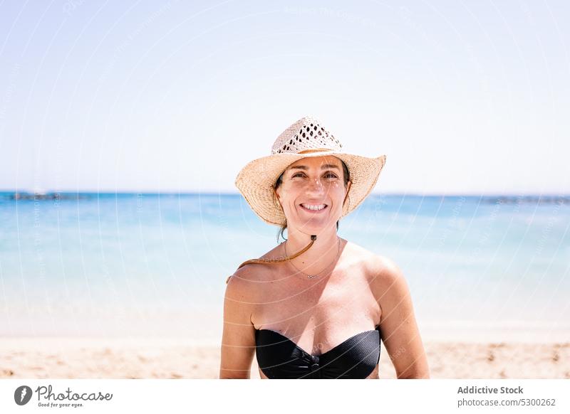 Smiling woman in hat standing on sandy beach sea smile summer shore style happy vacation cheerful young joy glad holiday positive water optimist travel resort