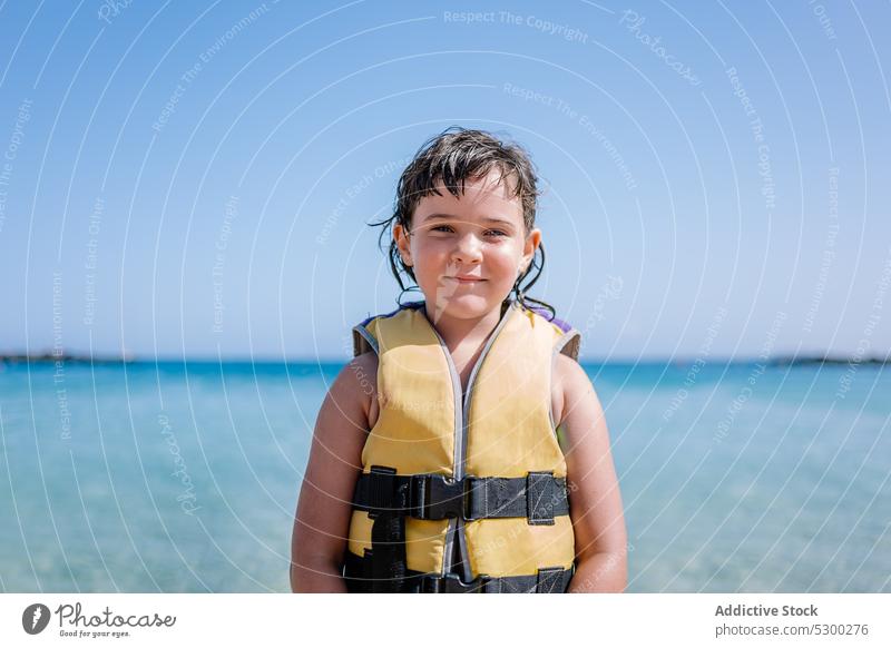 Smiling girl in safety swim jacket standing on beach child sea smile vacation sand shore positive ocean coast tourist summer holiday happy outdoors relax resort