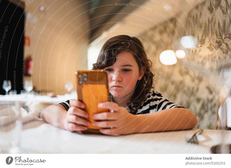 Focused girl watching video on smartphone in restaurant using concentrate online cafe gadget browsing device focus kid internet surfing mobile child interesting