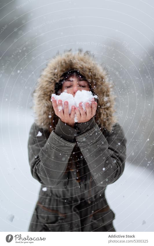 Content woman blowing snow from hands winter snowfall cold forest nature outerwear eyes closed weather female snowflake woods frost warm clothes season calm