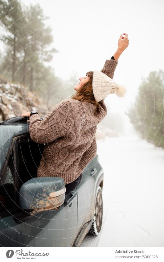 Unrecognizable woman leaning out car window in winter forest arm raised snow freedom bennie woods enjoy cold female nature weekend frost road vehicle season