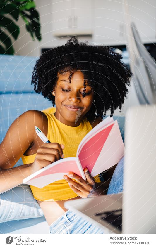 Content black woman taking notes in notepad take note smile cheerful write home notebook planner diary sofa african american young female positive casual couch