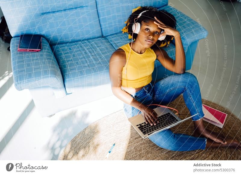 Pensive black woman working on laptop freelance headphones browsing typing thoughtful using home african american female young casual remote gadget project