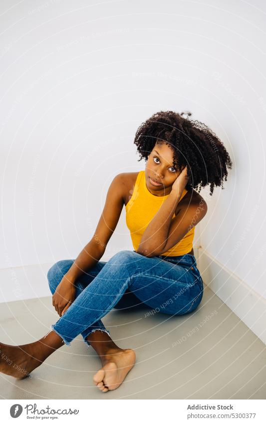 Calm black woman sitting on floor thoughtful calm pensive serious appearance curly hair hairstyle barefoot tranquil female young african american casual afro