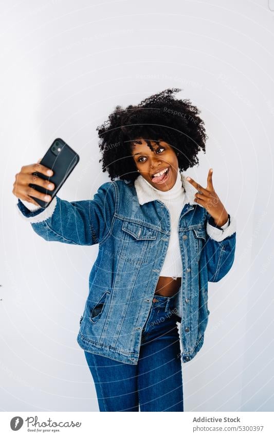 Joyful black woman taking selfie smartphone self portrait using show tongue afro grimace cheerful v sign happy african american ethnic hairstyle female gesture