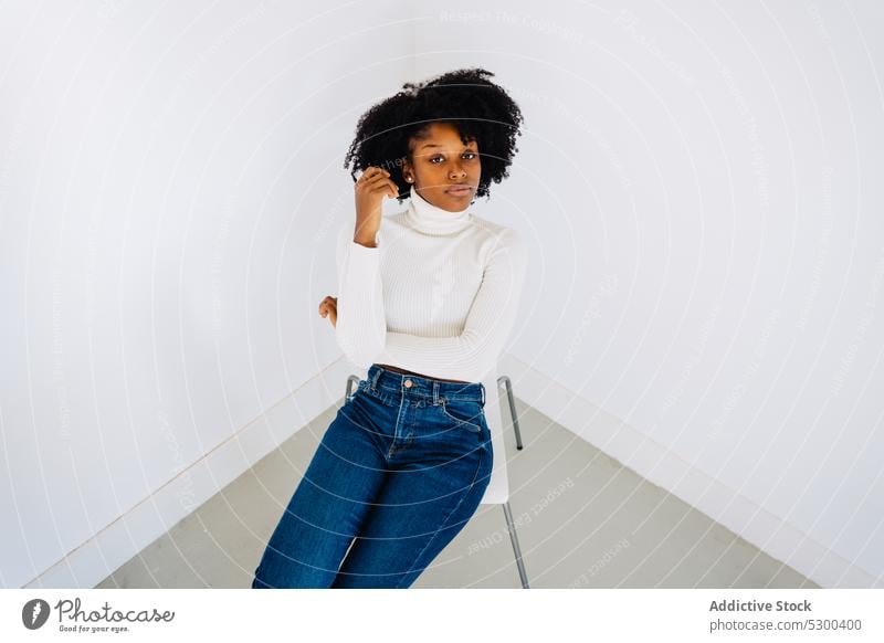 Trendy black woman sitting on chair fashion studio style confident model outfit serious trendy female african american slim young appearance posture carefree