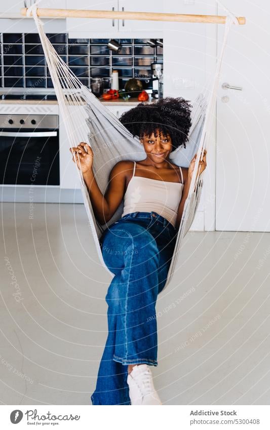 Content black woman resting on hammock home hang kitchen smile relax afro comfort happy african american young female casual positive curly hair hairstyle enjoy
