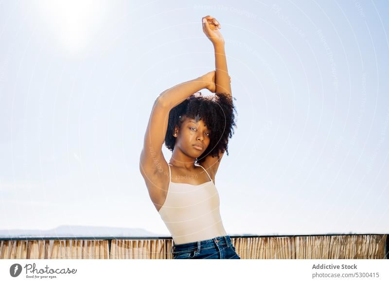 Slim black woman stretching arms style confident casual balcony curly hair afro tranquil young female african american outfit trendy brunette relax calm posture