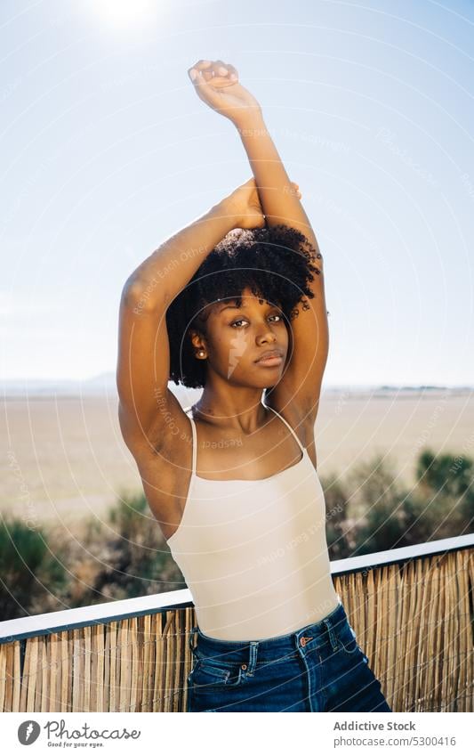 Slim black woman stretching arms style confident casual balcony curly hair afro tranquil young female african american outfit trendy brunette relax calm posture