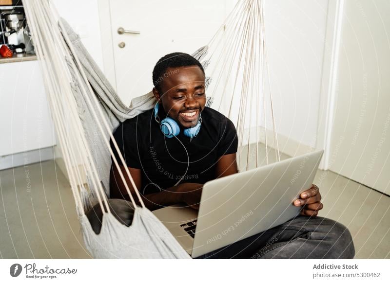 Positive black man with headphones using laptop freelance smile telework browsing home remote male african american cheerful ethnic casual happy device gadget