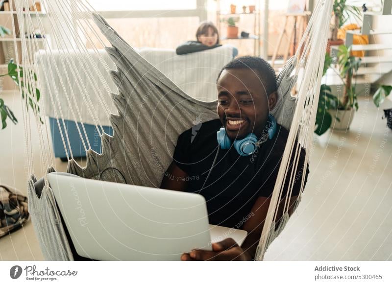 Positive black man with headphones using laptop freelance smile telework browsing home remote male african american cheerful ethnic casual happy device gadget