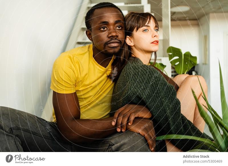 Pensive diverse couple hugging on stairs relationship love embrace staircase together young multiethnic multiracial cuddle affection casual plant boyfriend