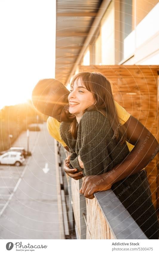 Joyful diverse couple hugging on balcony cheerful smile sunset love relationship together house happy railing terrace boyfriend multiethnic embrace multiracial