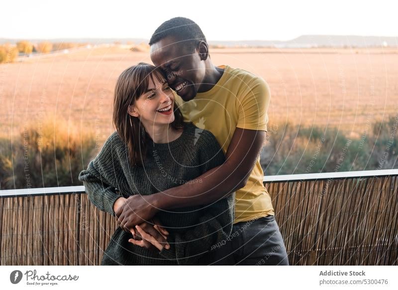 Joyful diverse couple hugging on balcony cheerful smile sunset love relationship together house happy railing terrace boyfriend multiethnic embrace multiracial