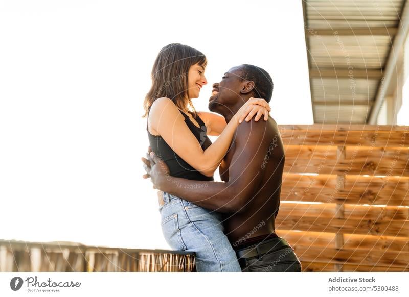 Positive multiethnic couple cuddling on terrace laugh embrace together cheerful balcony love hug happy relationship house multiracial diverse romantic smile