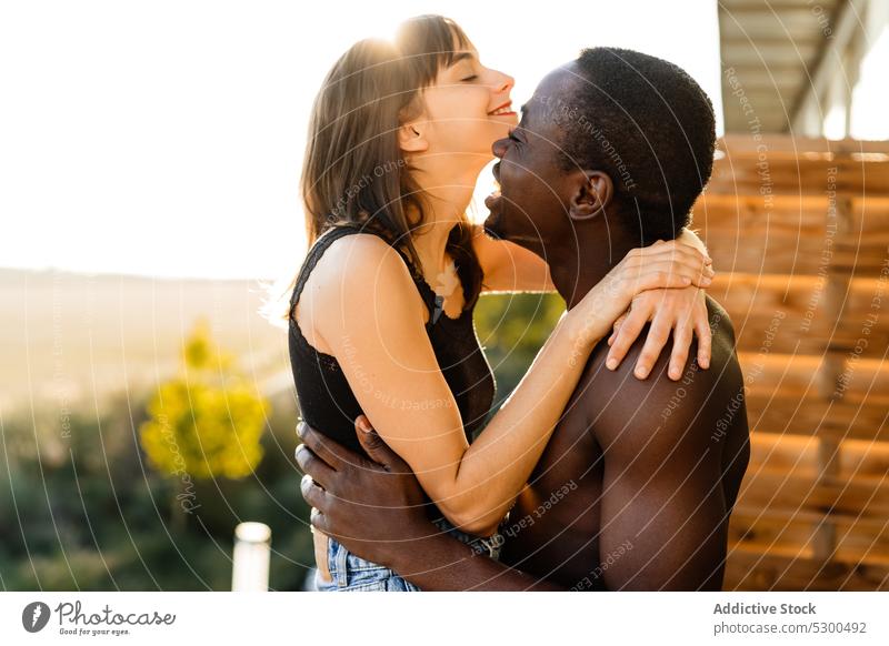 Positive multiethnic couple cuddling on terrace laugh embrace together cheerful balcony love hug happy relationship house kiss multiracial eyes closed diverse